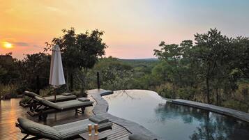 A poolside area with lounge chairs and a table, surrounded by lush greenery and a view of the landscape.