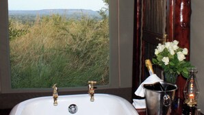 A bathroom with a large window offering a view of a grassy landscape and distant hills.