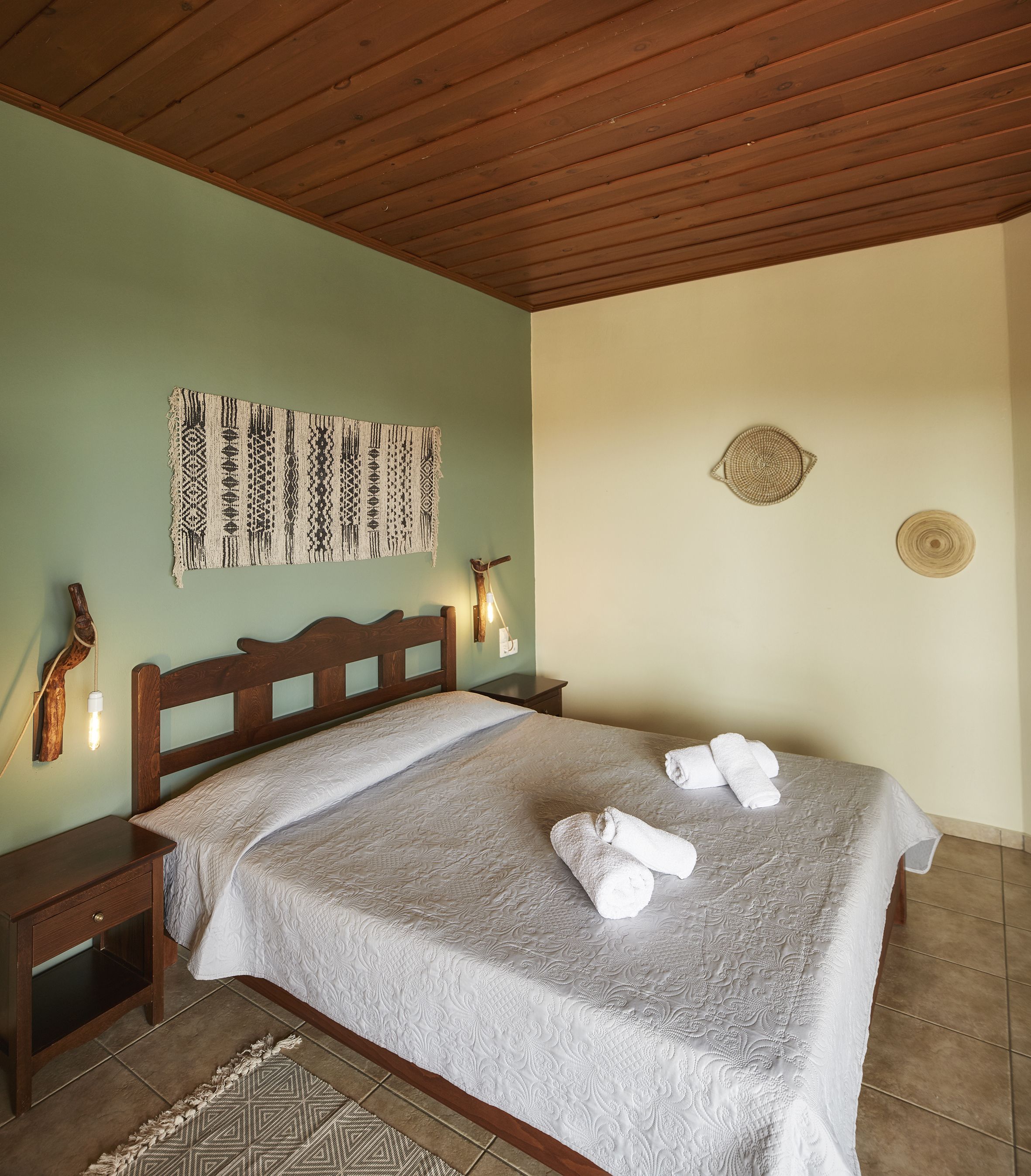 Una cama bien tendida con una colcha estampada, dos adornos en la pared y un cabecero de madera.