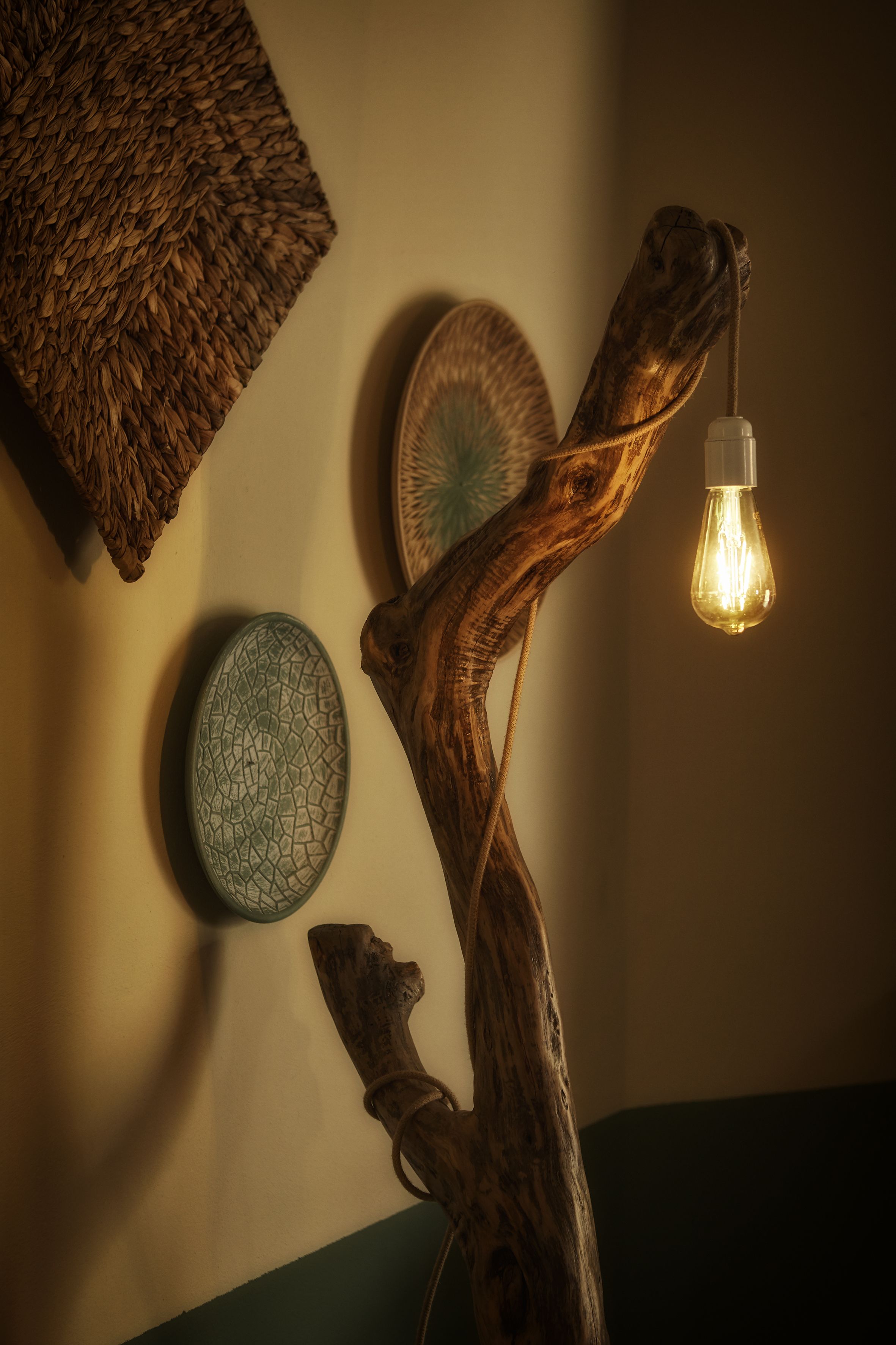 En vägg med en vävd textil, en dekorativ tallrik och en gren med en glödlampa.