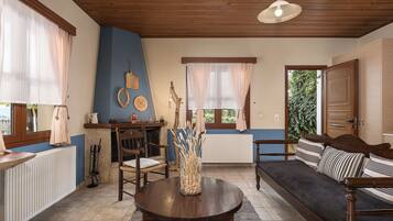 Una sala de estar con chimenea, techo de madera, un sofá, una mesa de comedor y una ventana con cortinas.