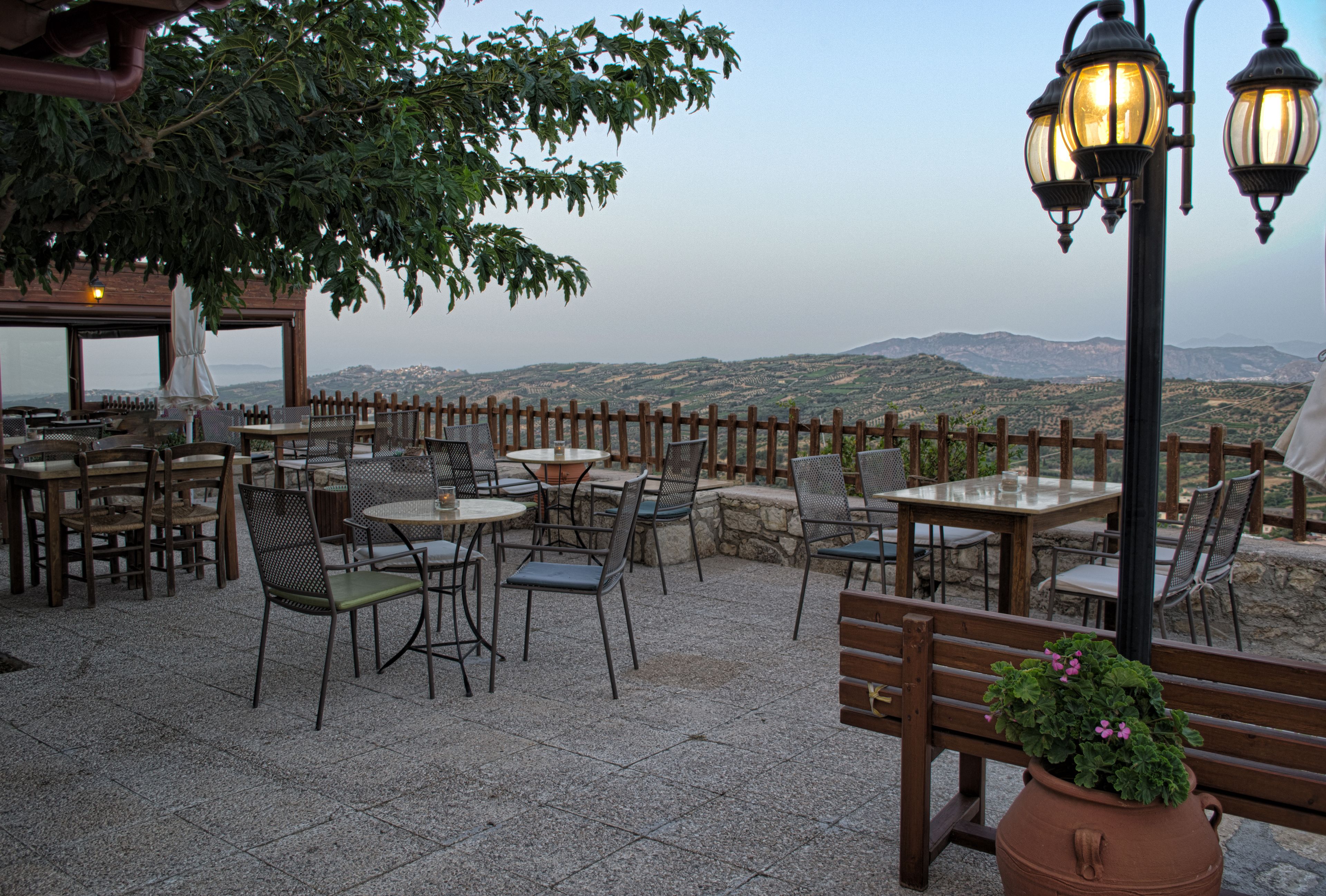 Un patio al aire libre con mesas y sillas, un cerco de madera y vistas a colinas distantes.