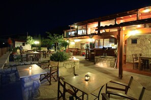An outdoor patio area with stone tables and wooden chairs, a stone fireplace, and a wooden pergola structure. - Earino (Heraklion)