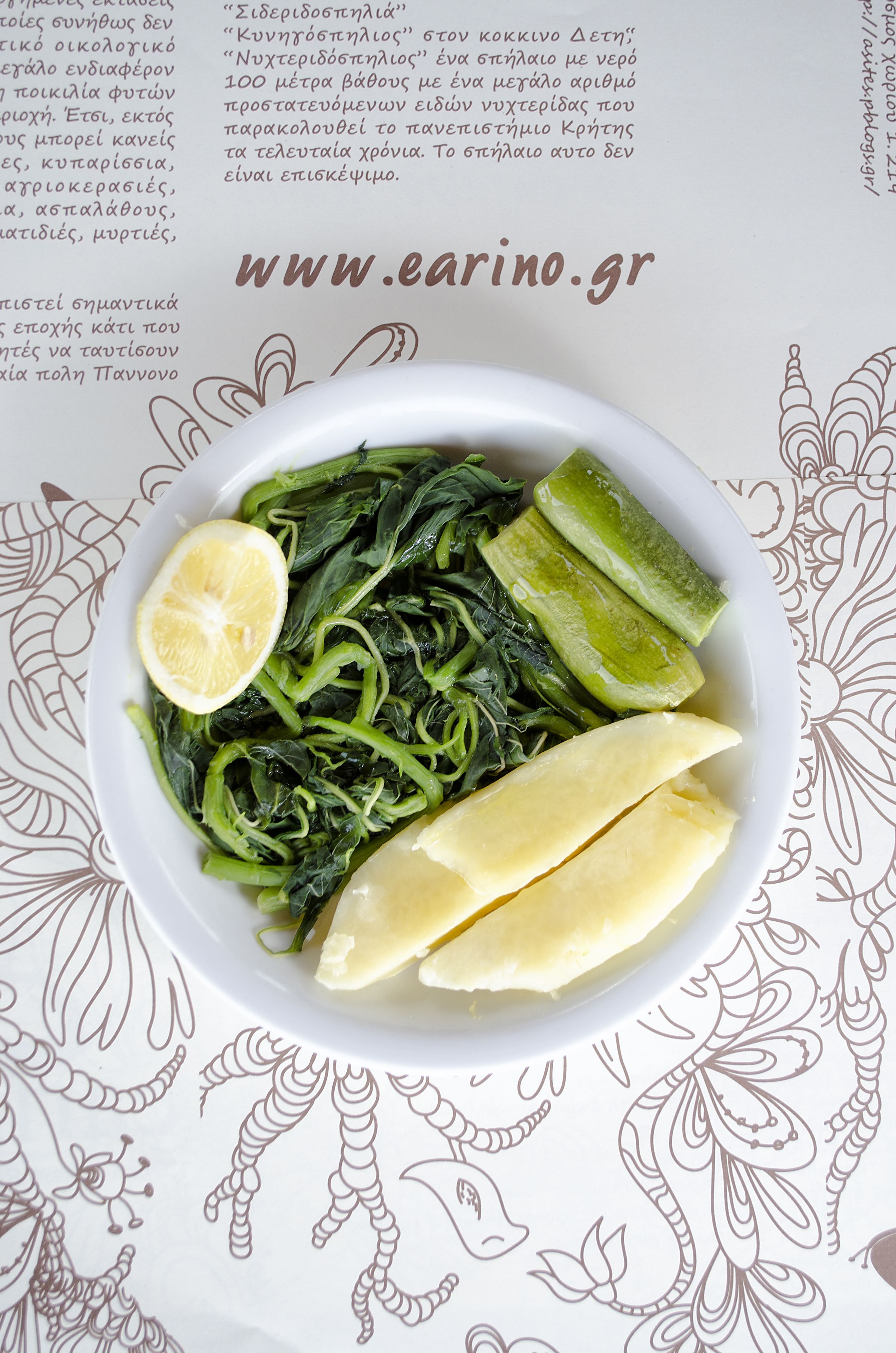 A plate of greens and pickles with lemon slices on a patterned tablecloth.