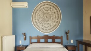 A bedroom with a wooden ceiling, a round wall hanging, a bed with two towels, a radiator, and bedside tables. - Earino (Heraklion)