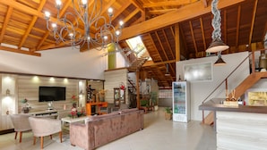 A spacious living area with a high ceiling, a large chandelier, a television, a sofa, and a refrigerator. - Zermatt Hotel (Gramado)