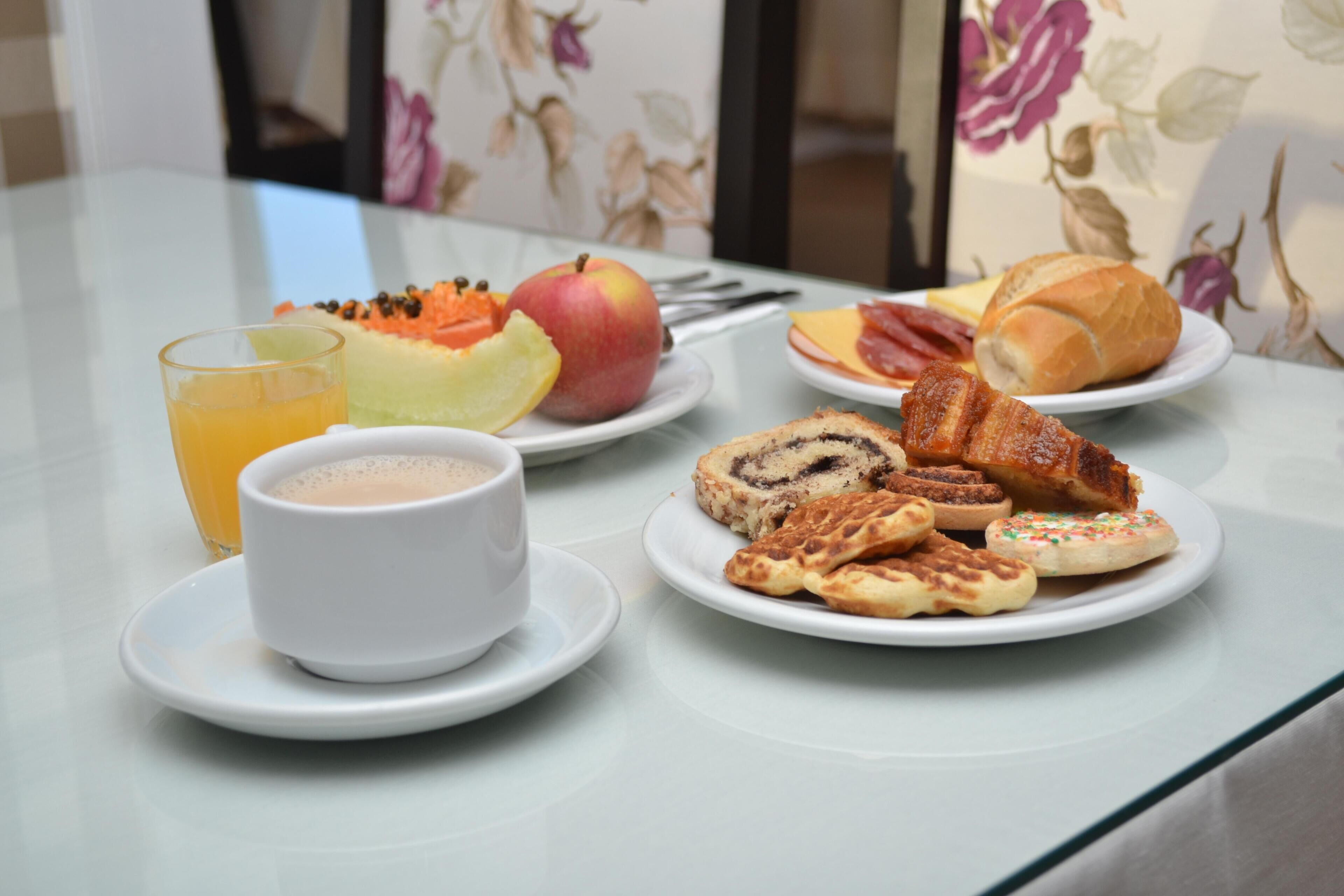 Una mesa de desayuno con platos de comida, un vaso de jugo de naranja y una taza de café.