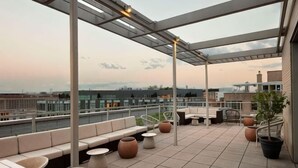 En tagterrasse med siddepladser, en plantekasse og udsigt over bybilledet.