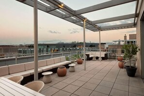 A rooftop terrace with seating, a potted plant, and a view of the cityscape.