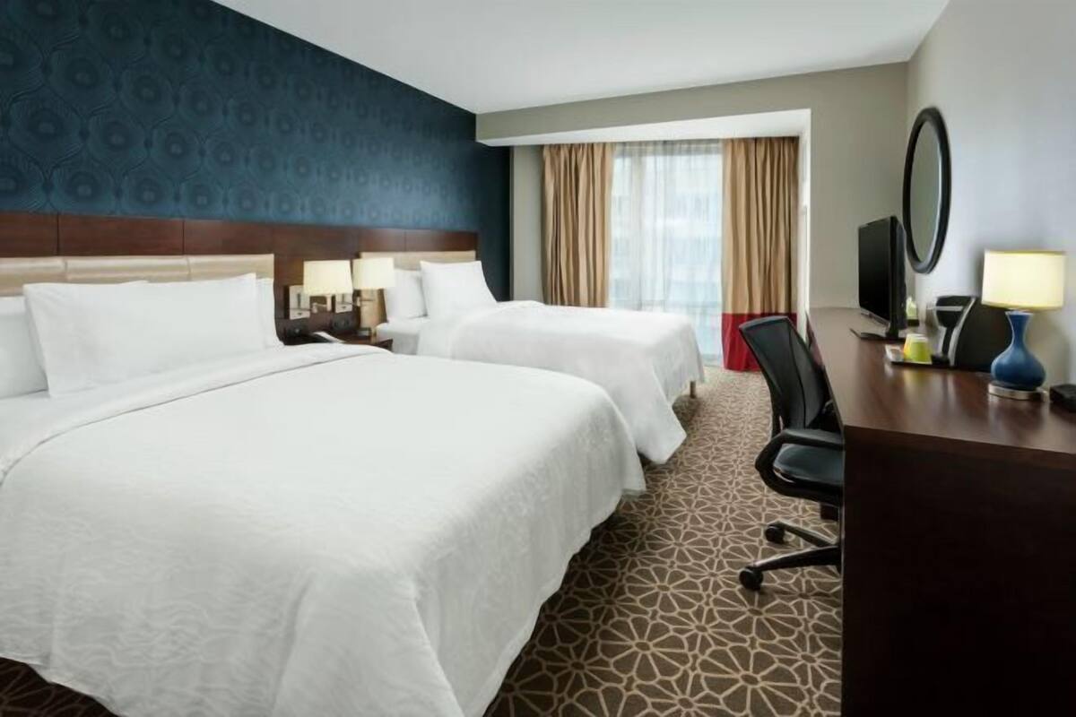 A hotel room with two beds, a desk, a chair, a TV, and a window with curtains.