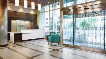 Uma área de recepção com design moderno, com balcão de atendimento, espaço para sentar e grandes janelas que permitem entrada de luz natural.