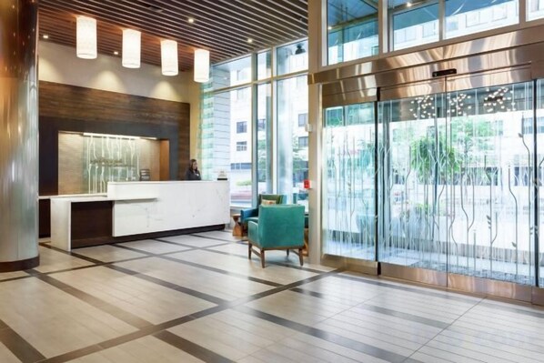 Un área de recepción con diseño moderno, que incluye un mostrador de recepción, zona de estar y ventanas amplias que permiten la entrada de luz natural.