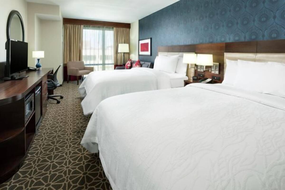 A hotel room with two beds, a desk with a TV, a chair, and a patterned carpet.