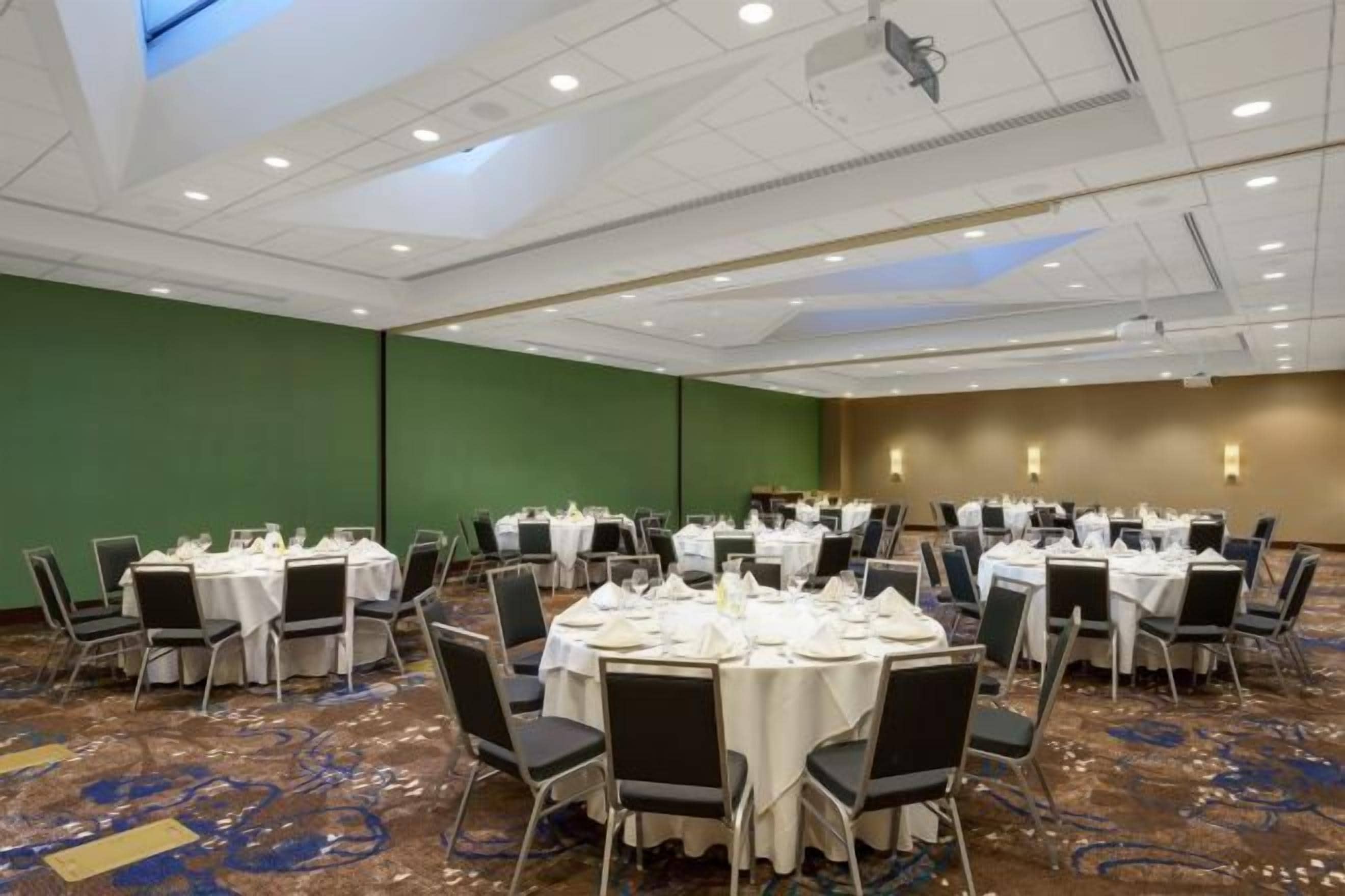 Un salón de conferencias con mesas redondas, sillas y suelo alfombrado.