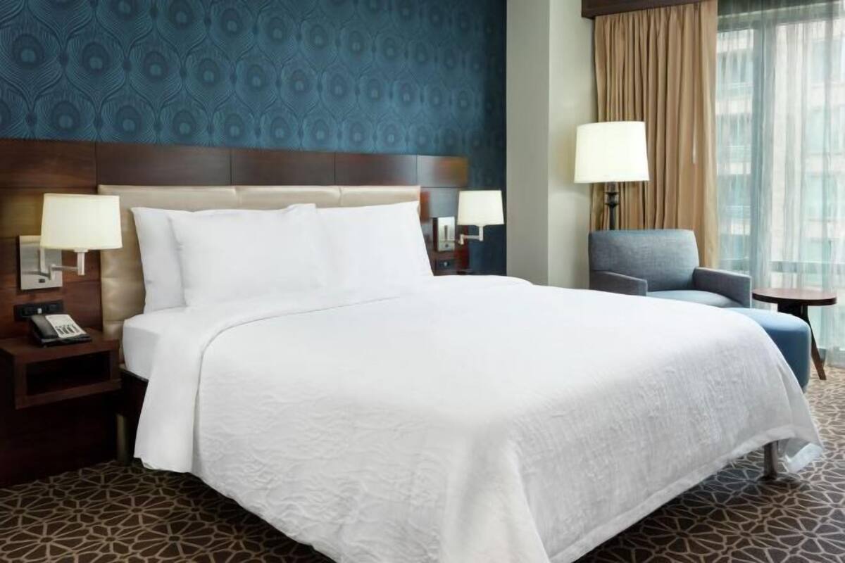 A hotel room with a large bed, two bedside tables with lamps, a chair, and a window with curtains.