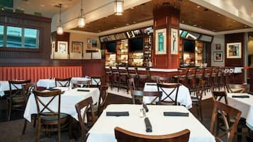 Um restaurante com várias mesas e cadeiras, um espaço de bar e teto de madeira.