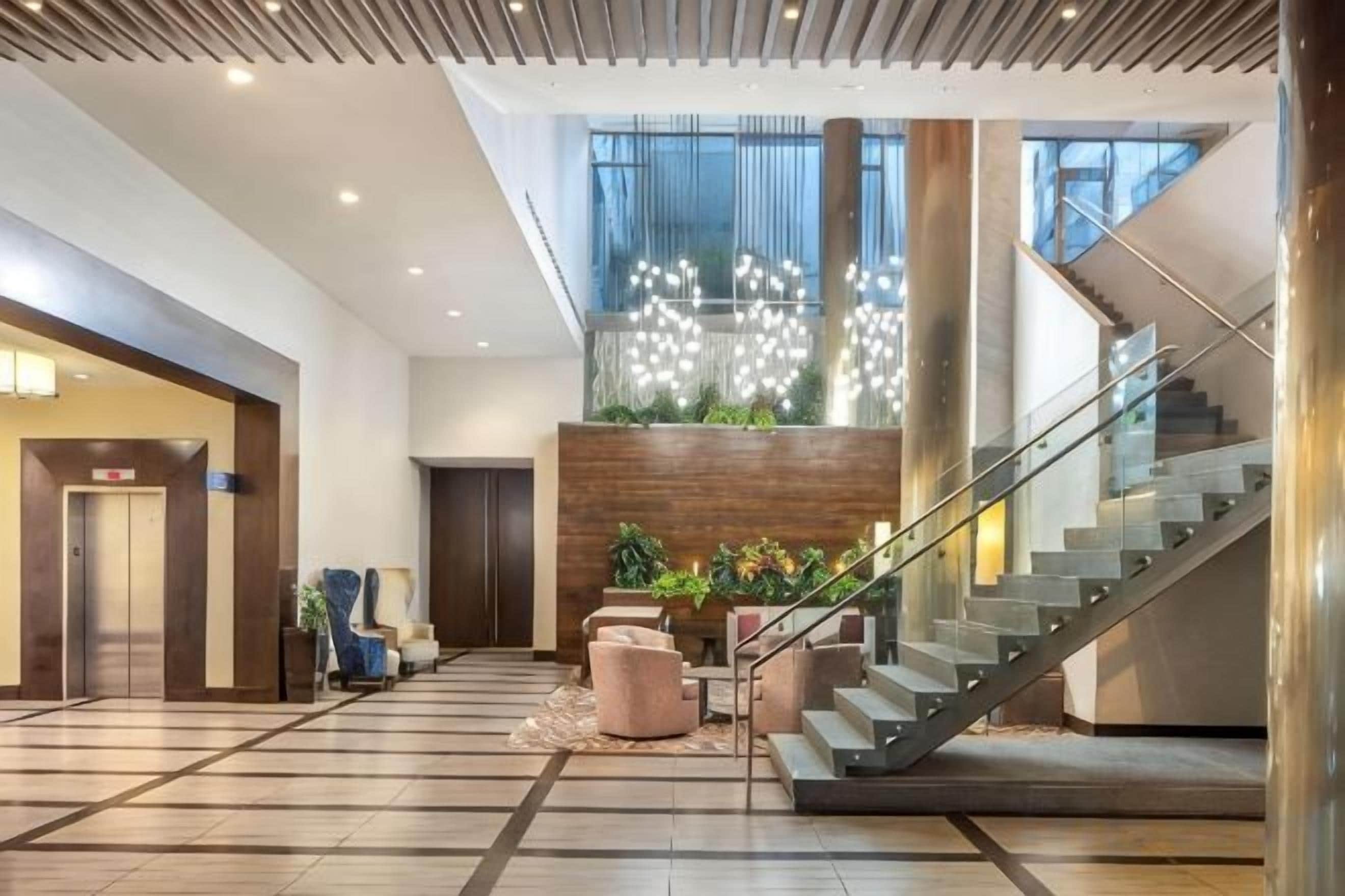 A modern hotel lobby with a staircase, seating area, and a reception desk.
