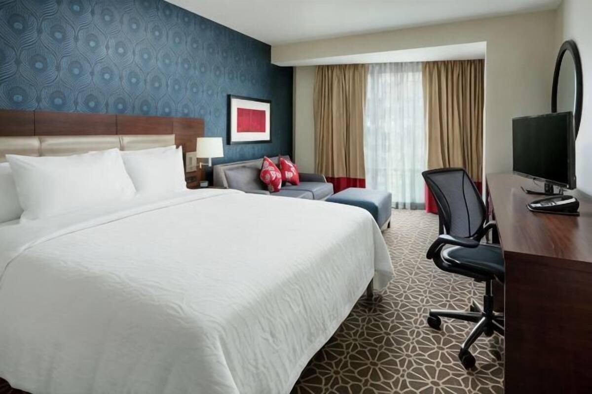 A hotel room with a large bed, a desk with a computer, a chair, and a TV.