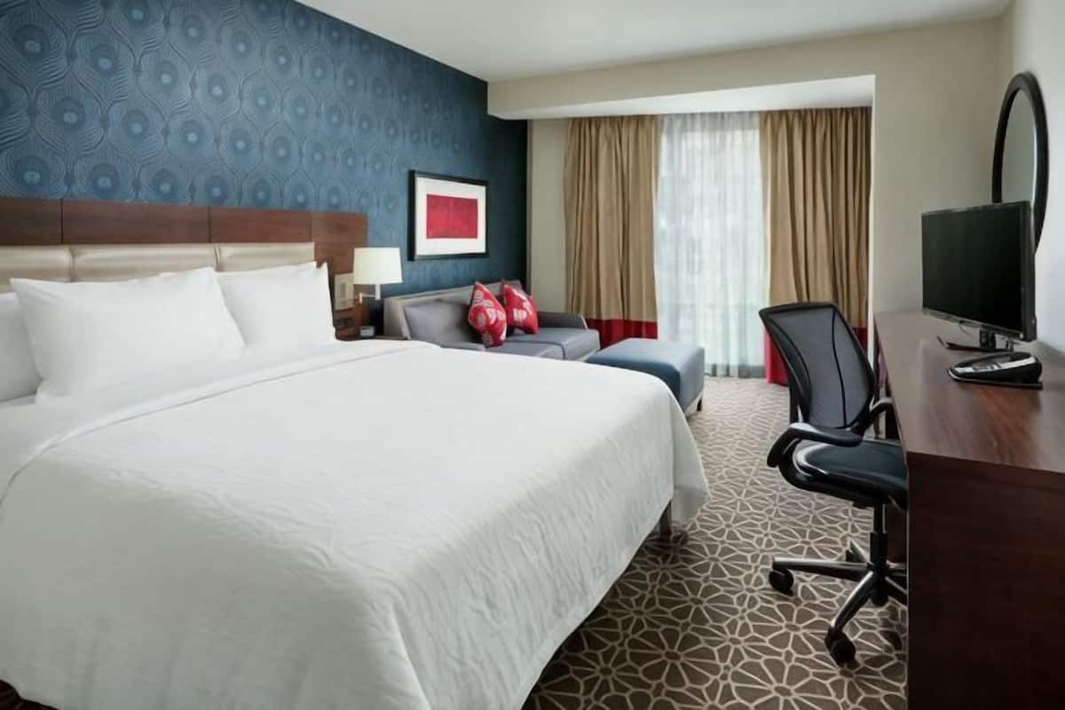 A hotel room with a large bed, a desk with a computer, a chair, and a TV.