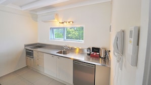A compact kitchen with a built-in dishwasher, a microwave, and a sink. There is a window above the sink with blinds, and a telephone on the wall to the right. - The Parnell Hotel and Conference Centre (Auckland)