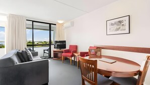 A modern hotel room with a sofa, dining table, chairs, a TV, and a large window offering a city view. - The Parnell Hotel and Conference Centre (Auckland)