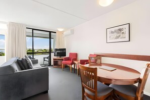 Une chambre d’hôtel moderne équipée d’un canapé, d’une table à manger, de chaises, d’un téléviseur et d’une grande fenêtre donnant sur la ville.
