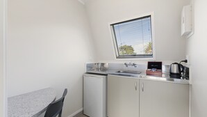 A compact kitchen with a small refrigerator, a sink, and a window with blinds. - The Parnell Hotel and Conference Centre (Auckland)