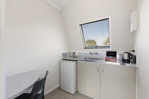 A compact kitchen with a small refrigerator, a sink, and a window with blinds. - The Parnell Hotel and Conference Centre (Auckland)