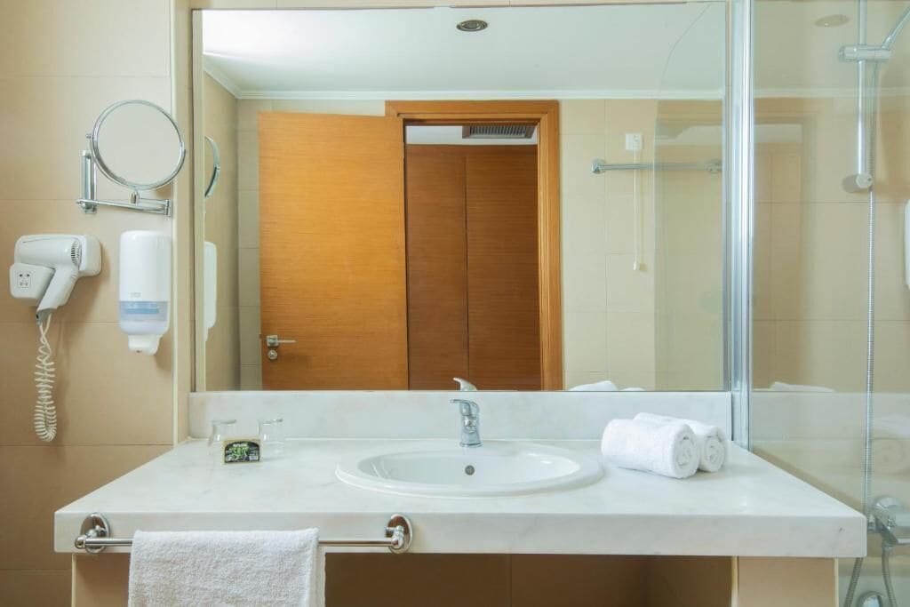 Un baño con lavamanos blanco, espejo, secador de pelo y toallero.