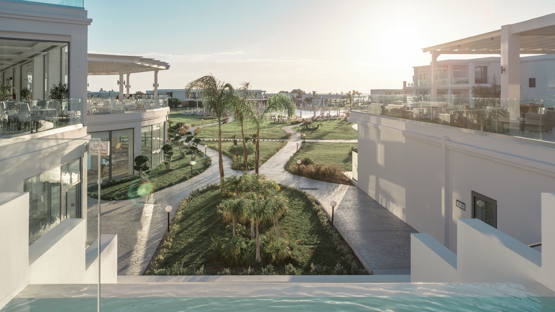 A modern hotel with a rooftop pool, a landscaped garden with a winding path, and a spa area.