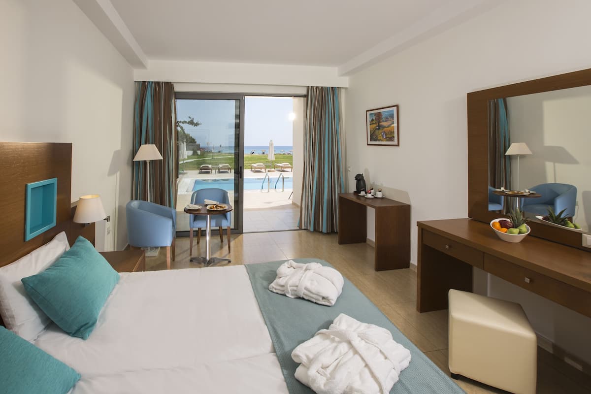 Une chambre d’hôtel comprenant un lit, un bureau, une chaise, une petite table et donnant sur la piscine et la plage.