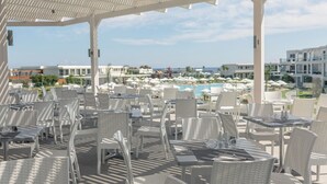 A covered outdoor dining area with white wicker furniture, overlooking a pool and resort buildings.