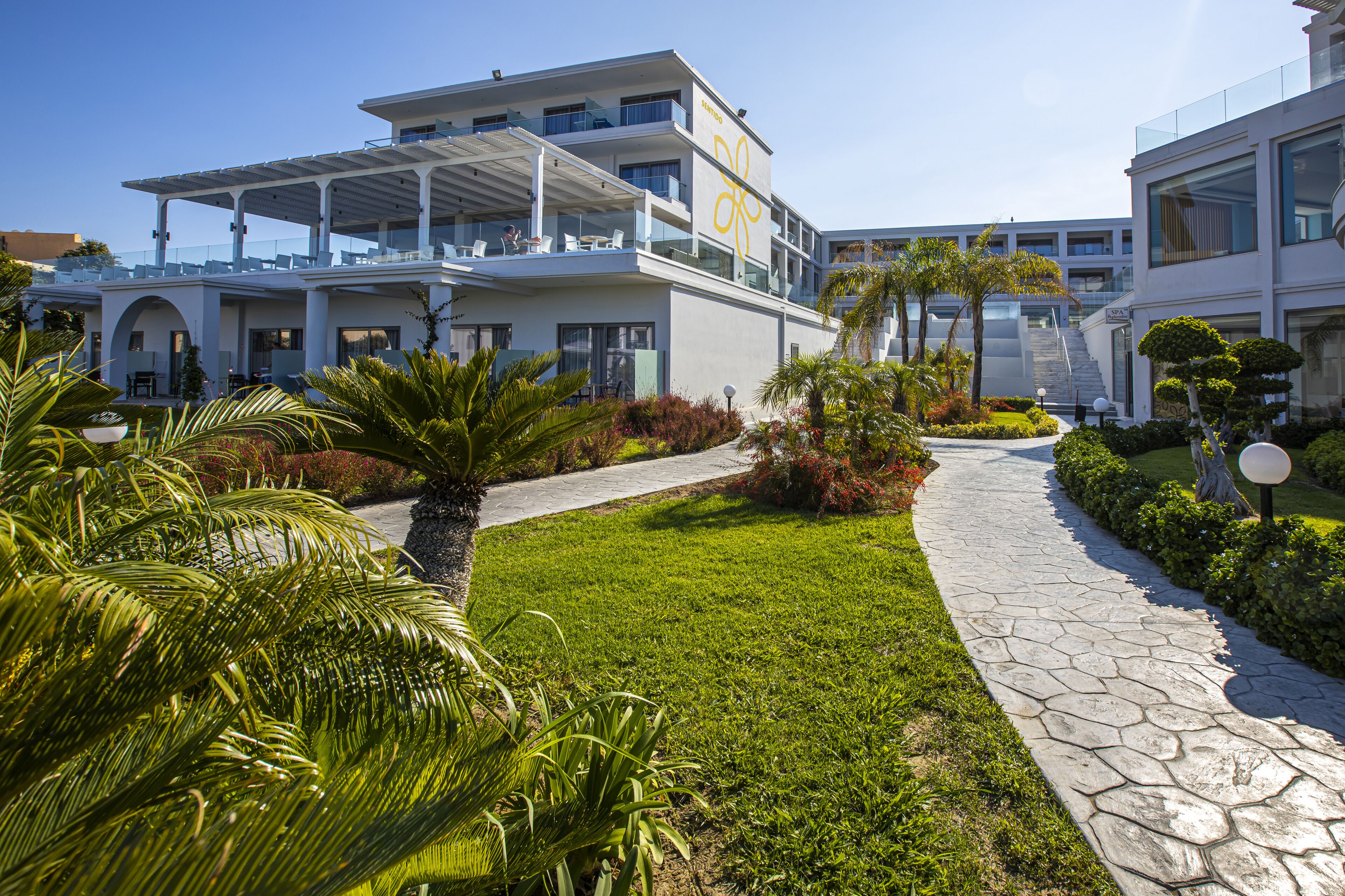 A modern hotel with a rooftop terrace, lush landscaping, and a stone pathway.