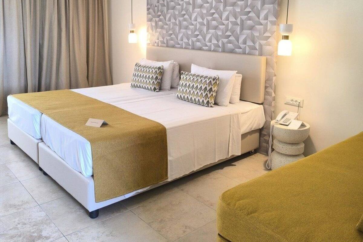 Une chambre d’hôtel avec un grand lit, une tête de lit ornée d’un motif géométrique, une table de chevet avec une lampe et une petite table ronde avec un téléphone.