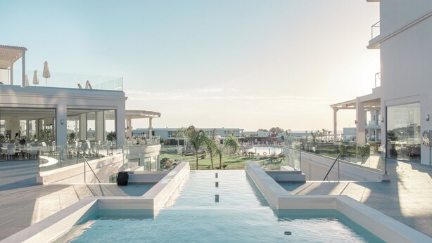 A rooftop pool area with glass balustrades, outdoor seating, and a view of the surrounding buildings. - Asterias Beach Resort (Rhodes)