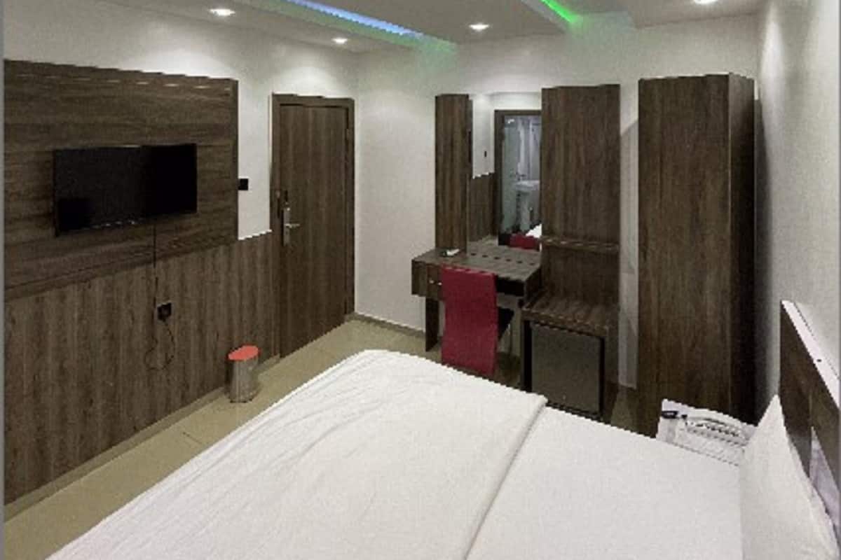 A modern hotel room with a large bed, a desk with a chair, a TV mounted on the wall, and wooden paneling on the walls.