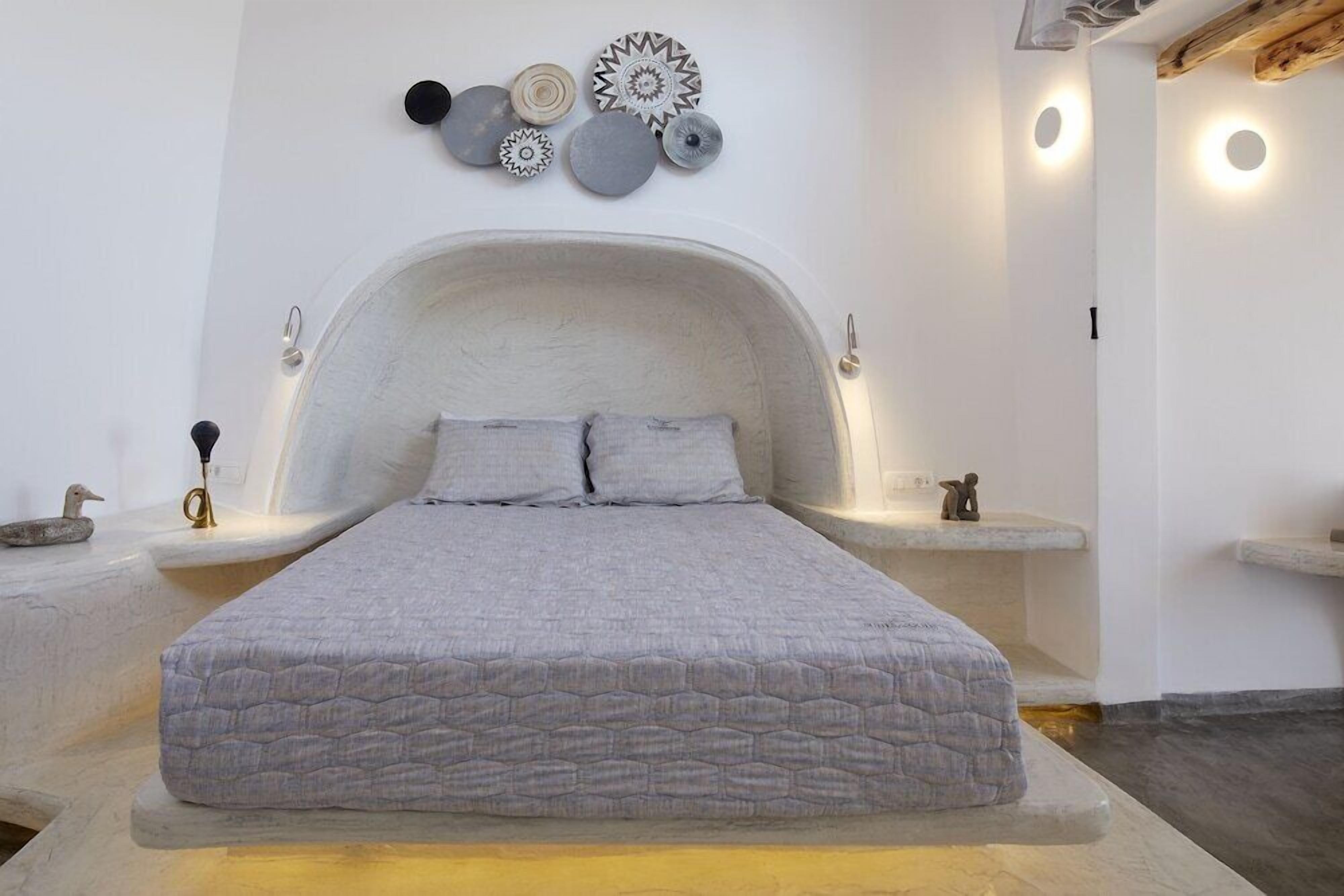 A bed with a textured gray mattress, a white headboard, and two pillows. There are wall-mounted decorative plates above the bed.