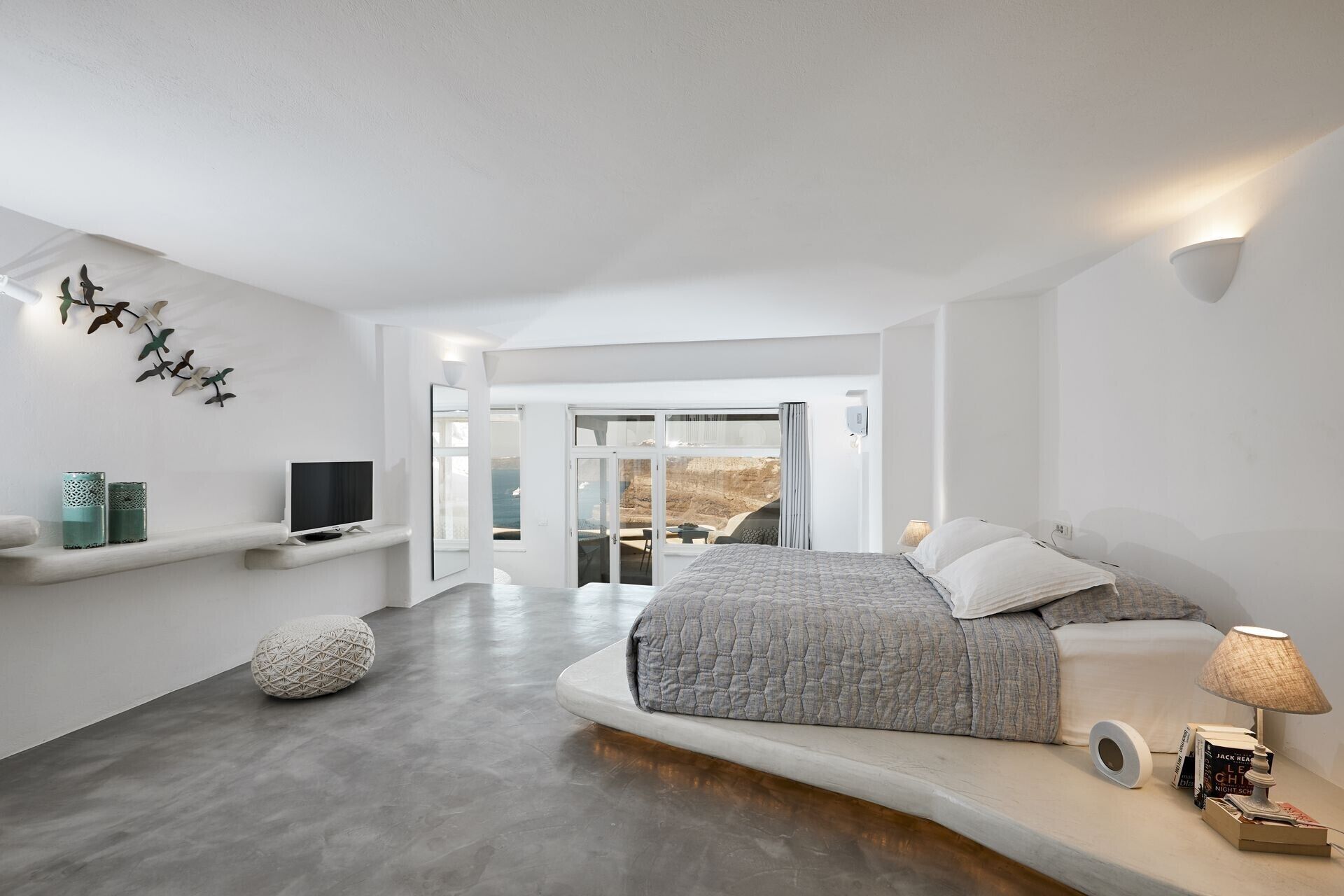 A modern bedroom with a large bed, a TV, and a view of the outdoors.