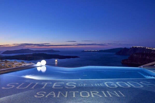 A luxurious infinity pool at Suites of the Gods Santorini with a clear view of the sea and distant mountains.