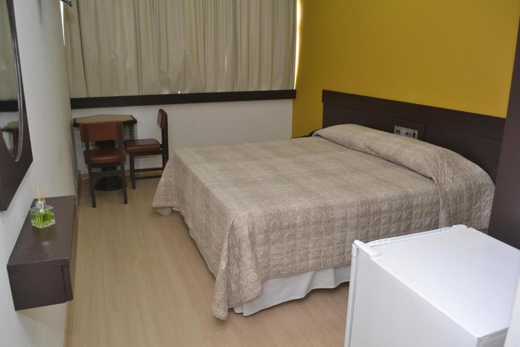 A hotel room with a bed, a desk, a chair, and a small table with a bottle.