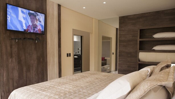 Un dormitorio moderno con una cama grande, un televisor montado en la pared y una estantería empotrada.