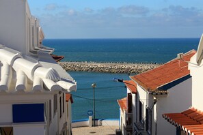 A coastal street with buildings, a rocky breakwater, and the sea in the background. - Villa Ana Margarida Residences (Mafra)