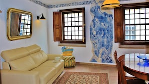 A room with a beige sofa, a patterned rug, a wooden dining table, and a blue tiled wall. - Villa Ana Margarida Residences (Mafra)