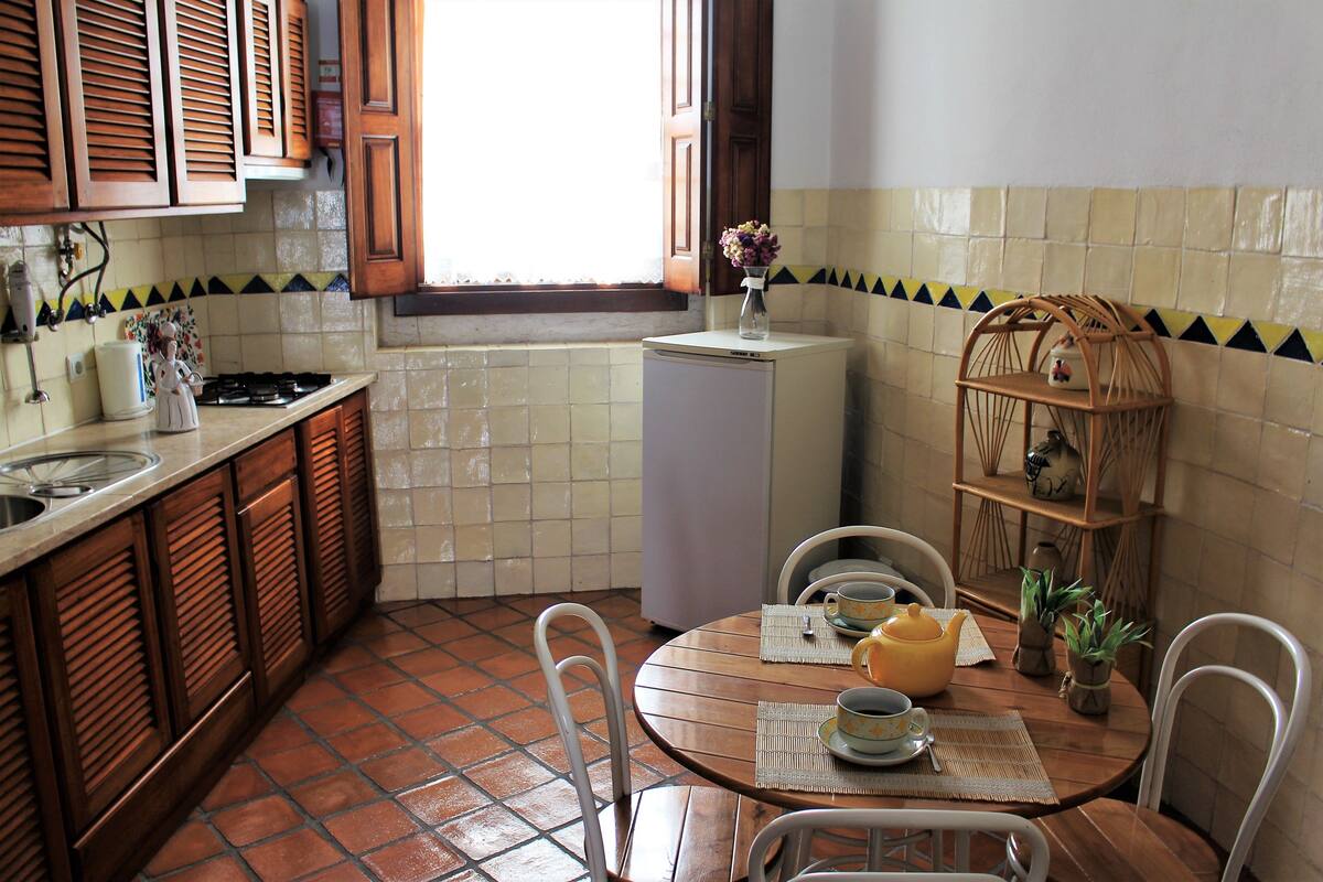 Een keuken met een eethoek, met een betegelde spatwand, houten kastjes, een koelkast en een eettafel met stoelen.