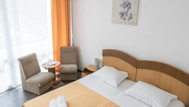 Una habitación de hotel con una cama grande, dos sillas, una mesita y un cuadro en la pared.