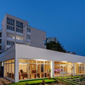 A modern hotel with a flat roof, large glass windows, and a green lawn area.