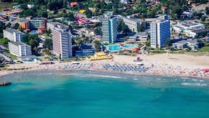 Vista aérea de una zona costera con varios edificios altos, una playa con numerosos sombrillas y una piscina.