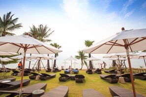 A beachside lounge area with multiple lounge chairs and umbrellas, palm trees, and a view of the sea. - Mövenpick Siam Hotel Na Jomtien Pattaya (Sattahip)