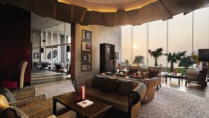 A spacious lounge area with wicker furniture, a coffee table, and a large window offering a view of the sea. - Mövenpick Siam Hotel Na Jomtien Pattaya (Sattahip)