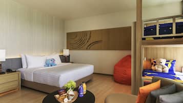 A hotel room with a bed, a nightstand, a bedside table, a round coffee table, a red bean bag, a sofa, and a bunk bed with a teddy bear.